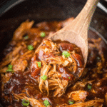 Wooden spoon lifting shredded crock pot bourbon chicken in thick glaze