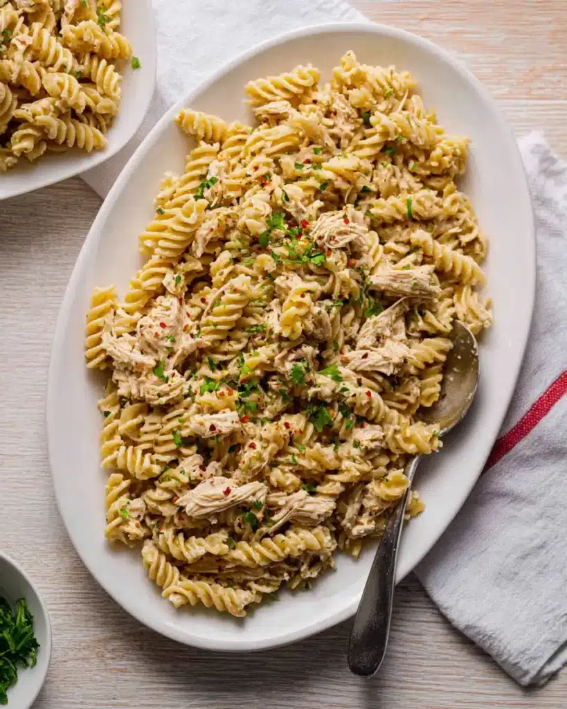 Creamy garlic parmesan chicken rotini pasta served on a white platter, topped with parsley and red pepper flakes