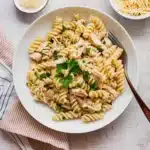 Creamy garlic parmesan chicken pasta with rotini noodles, served in a white bowl and topped with parsley, on a rustic wooden table