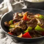 Bowl of crockpot pepper steak with bell peppers, onions, and glazed beef, served with white rice.