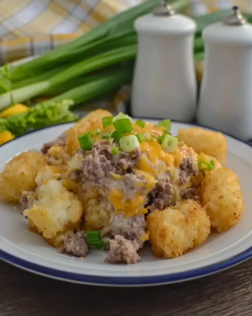 Side view of slow cooker cowboy casserole with tater tots, beef, cheese, and green onions on a white plate
