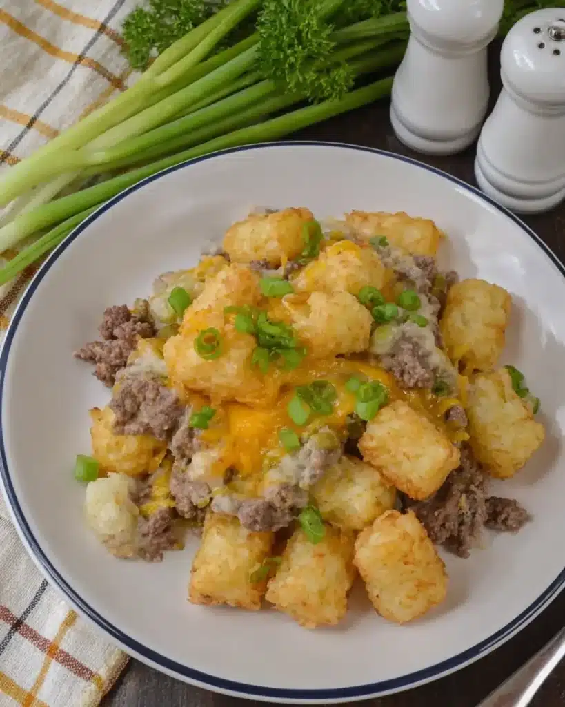 Overhead view of slow cooker cowboy casserole served with crispy tater tots, ground beef, melted cheese, and green onions on a white plate