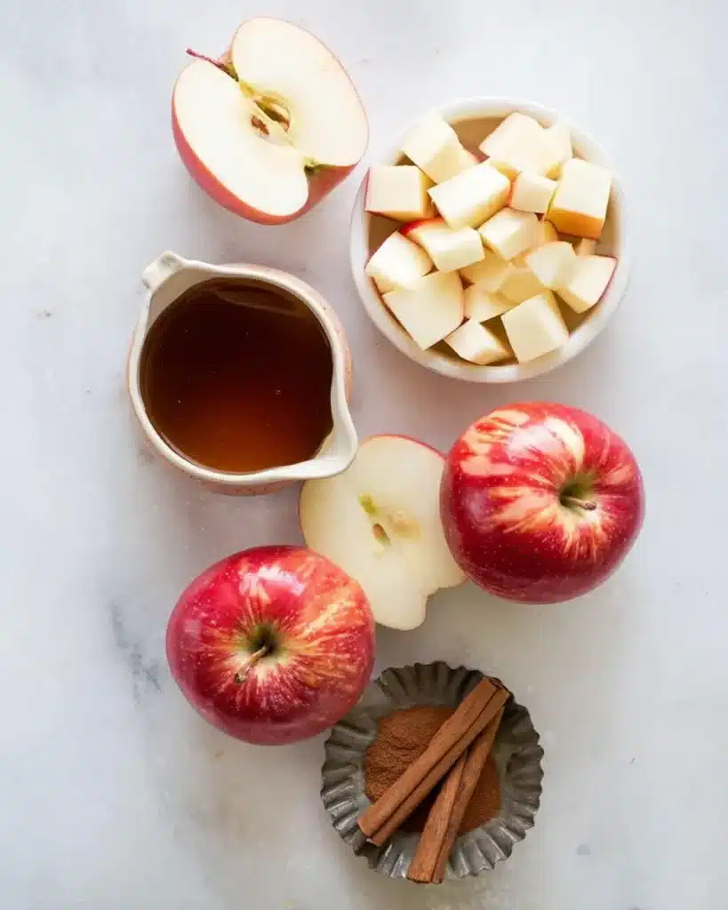 Ingredients for air fryer apples including fresh apples, cinnamon sticks, maple syrup, and diced apple cubes