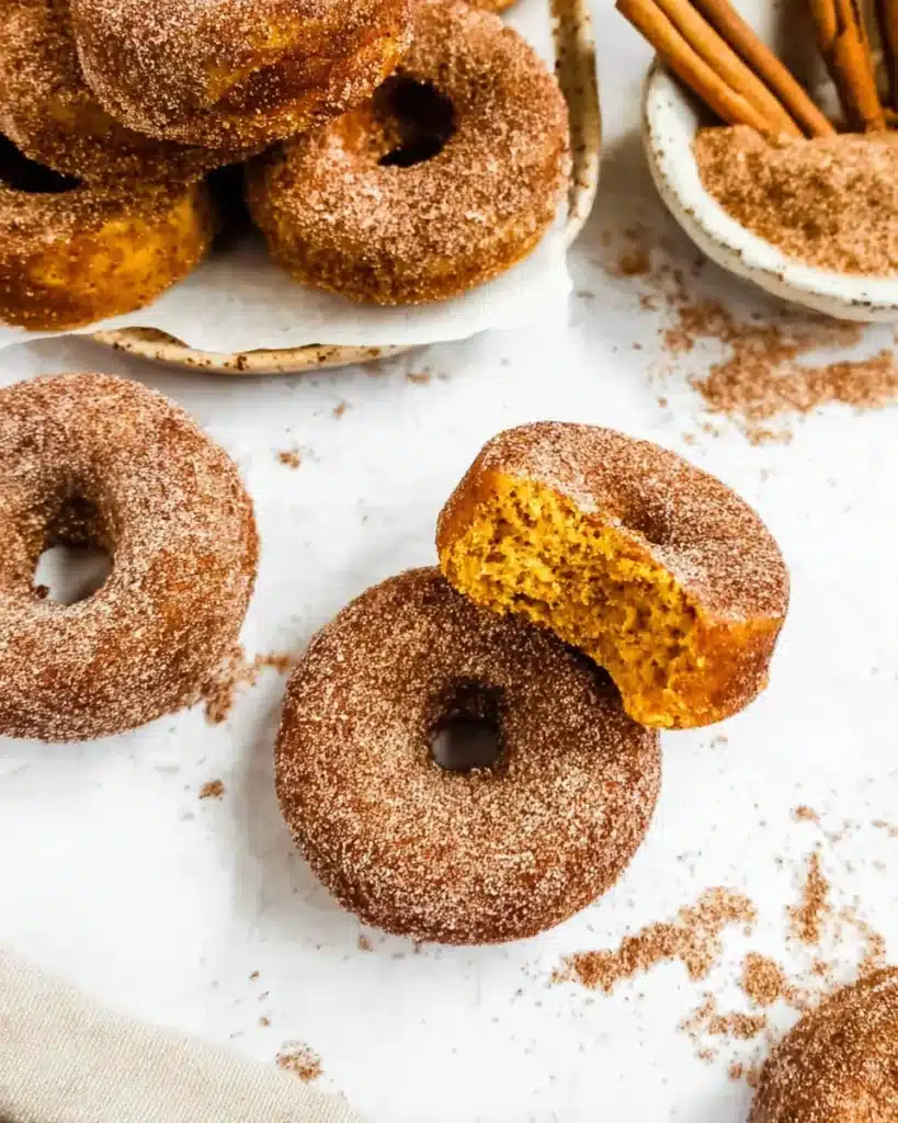 Flatlay of cinnamon sugar pumpkin donuts with one donut showing soft interior and cozy fall styling
