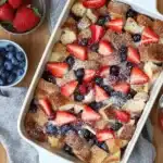 Overhead view of berry French toast casserole topped with strawberries and blueberries in a white baking dish, dusted with powdered sugar.