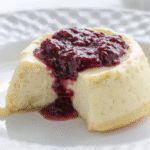 Keto cheesecake with a bite taken out, topped with berry compote on a white plate