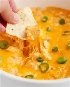 Close-up of creamy Buffalo chicken dip in a crock pot with melted cheddar cheese and tortilla chip scoop