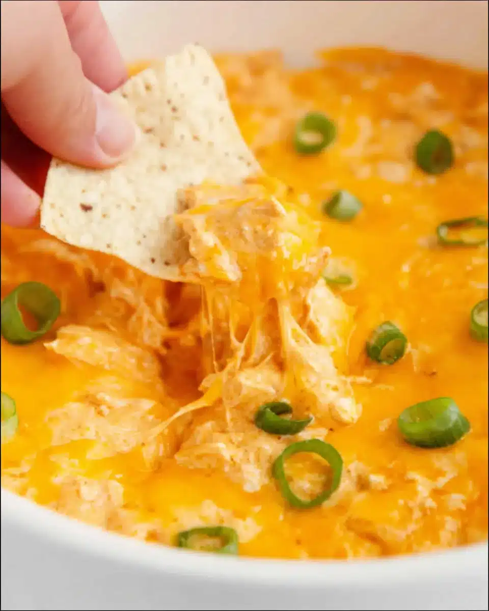 Close-up of creamy Buffalo chicken dip in a crock pot with melted cheddar cheese and tortilla chip scoop