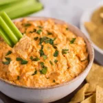 Crockpot Buffalo Chicken Dip served with a fresh celery stick and garnished with chopped herbs