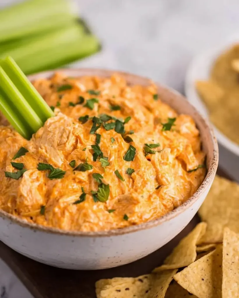 Crockpot Buffalo Chicken Dip served with a fresh celery stick and garnished with chopped herbs