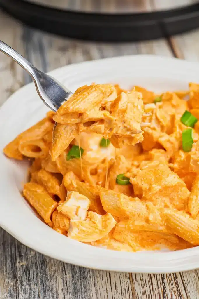 Forkful of creamy Crock Pot Buffalo Chicken Pasta with cheese sauce and chicken on a white plate