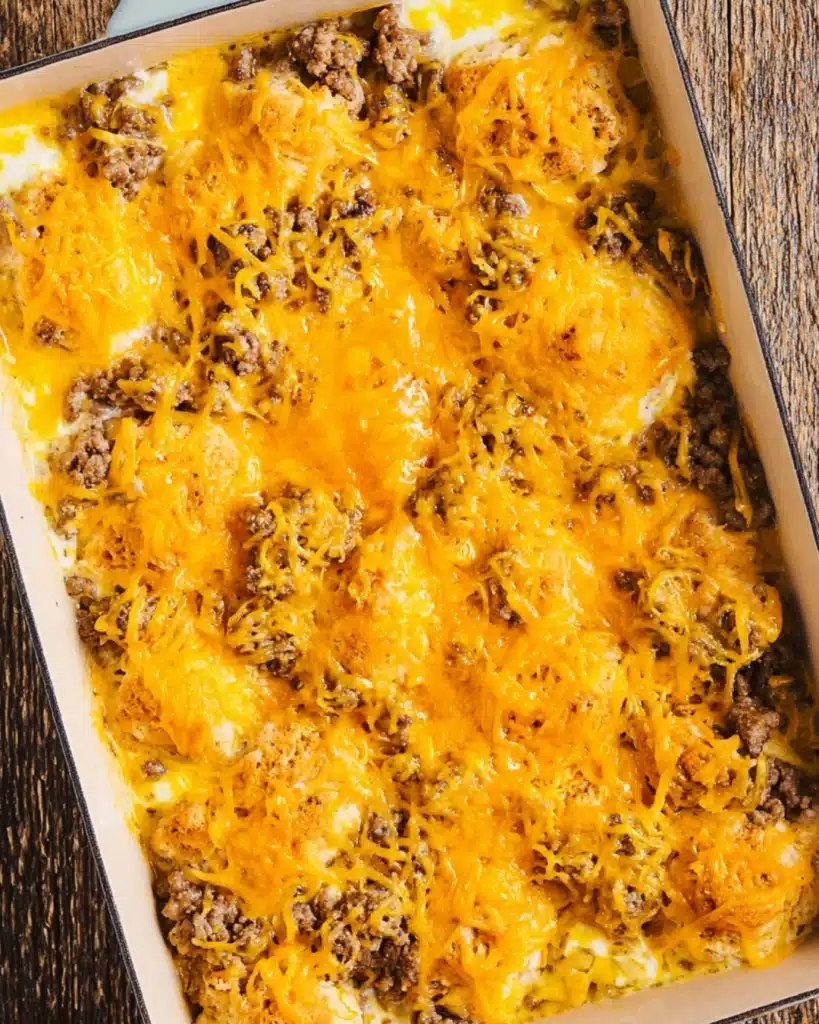 Shredded cheddar cheese layered over sausage and biscuit dough in casserole dish