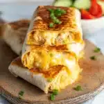 Crispy cheesy garlic chicken wraps stacked on a plate with melted cheese and green onions