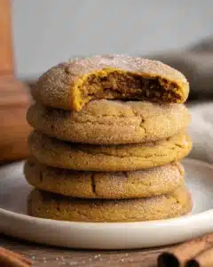 Stack of chewy pumpkin cookies on a white plate, warm golden-brown color with sugar coating, rustic background.