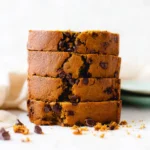 Stack of moist chocolate chip pumpkin bread slices with melty chocolate chips on a ceramic surface.