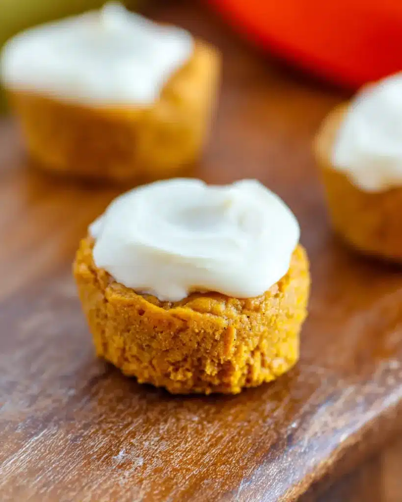 Close-up of a moist flourless pumpkin muffin with creamy frosting on rustic wood table