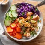Bang Bang Chicken Bowls with creamy sauce, sautéed veggies, crispy chicken, and rice in a white bowl