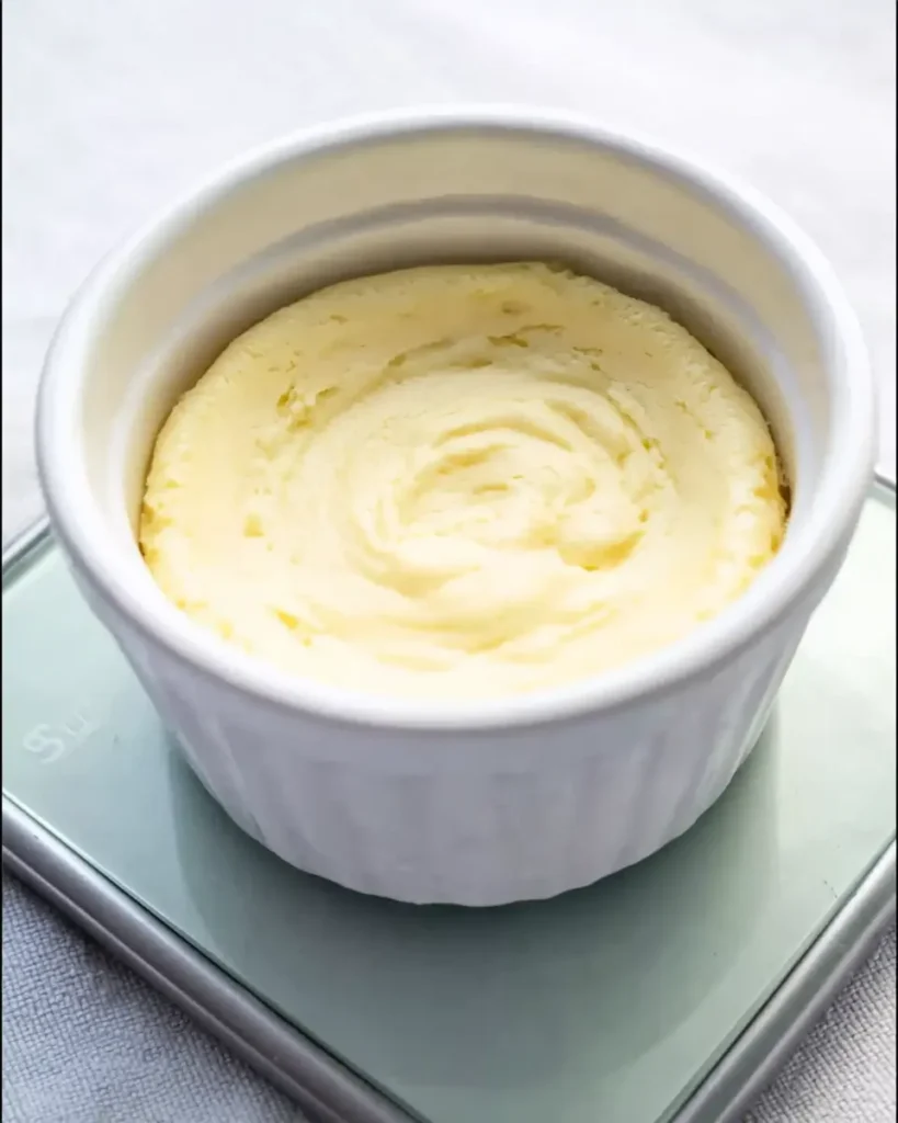 Cooked keto cheesecake in a white ramekin with smooth fluffy top resting on a digital scale