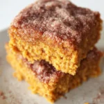 Stacked pumpkin snack cake squares with cinnamon sugar topping on a white plate