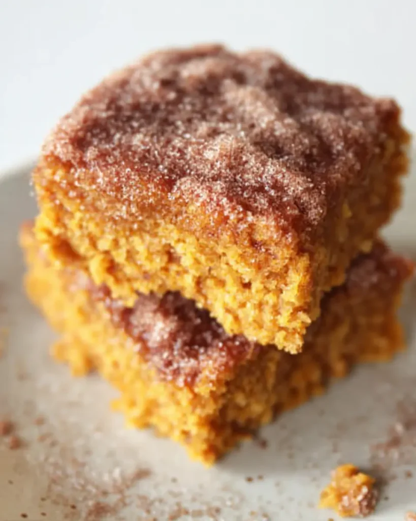 Stacked pumpkin snack cake squares with cinnamon sugar topping on a white plate