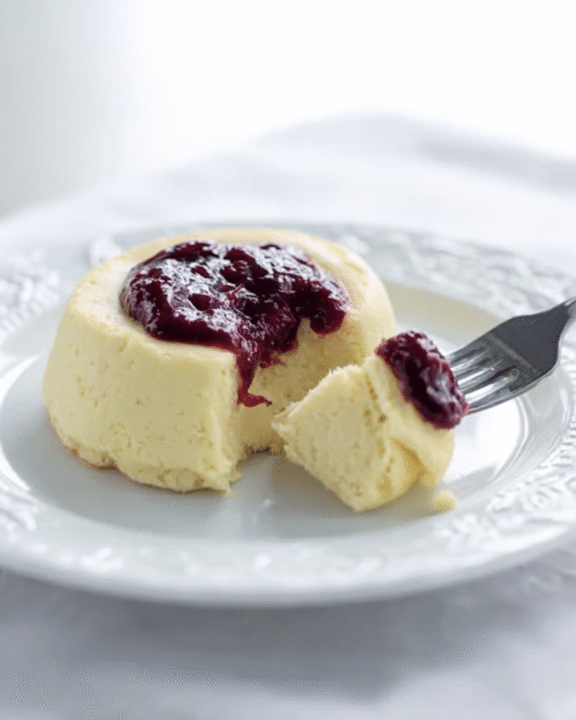 Partially eaten keto cheesecake with a berry topping on a white plate, fork lifting a creamy bite