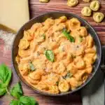 Bowl of creamy CrockPot chicken tortellini with tomato sauce, basil, and Parmesan on a rustic wooden table