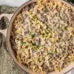 Creamy ground beef stroganoff in a skillet with egg noodles and fresh parsley, viewed from above on a light surface.