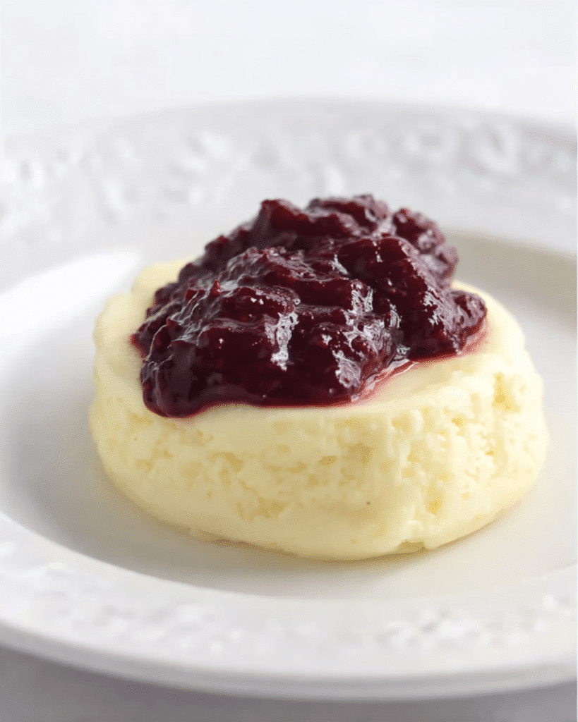Keto cheesecake with berry compote topping on a white plate, soft and creamy texture with a thick fruit sauce