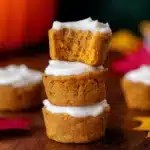 Stack of moist flourless pumpkin muffins with creamy white frosting on rustic wooden table