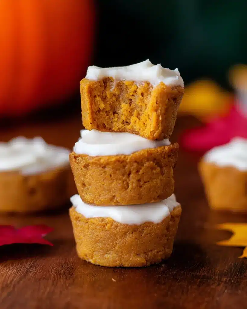 Stack of moist flourless pumpkin muffins with creamy white frosting on rustic wooden table