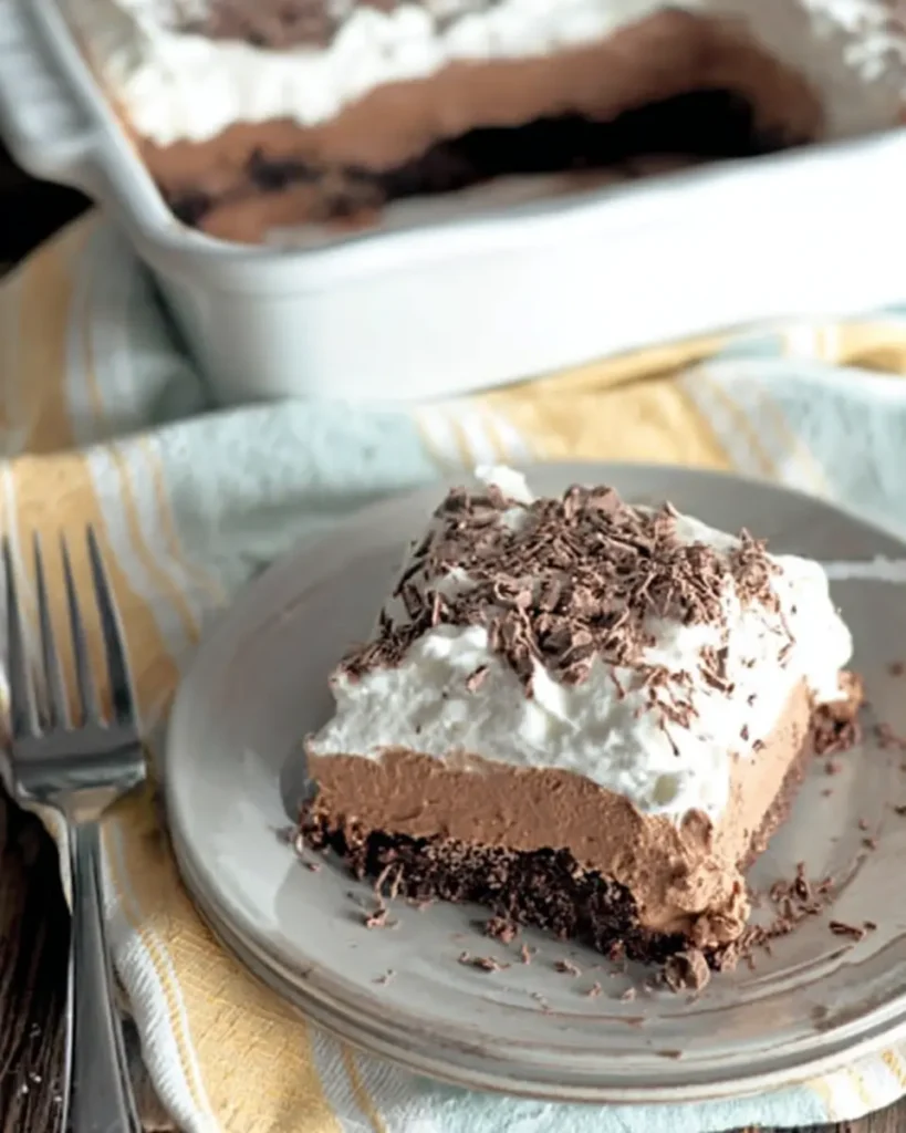 Close-up of French Silk Brownie on a ceramic plate with baking dish in background.
