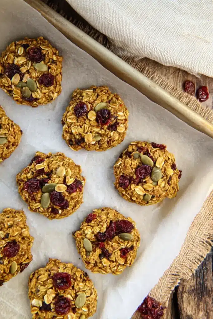 Top-down view of baked pumpkin oat breakfast cookies with cranberries and seeds on a baking tray