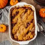 Baked pumpkin cobbler in a ceramic dish with golden crust and caramel edges, styled with mini pumpkins and fall decor