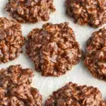 Close-up of gluten-free no bake cookies with a chunky oat texture and glossy chocolate coating on a light background.