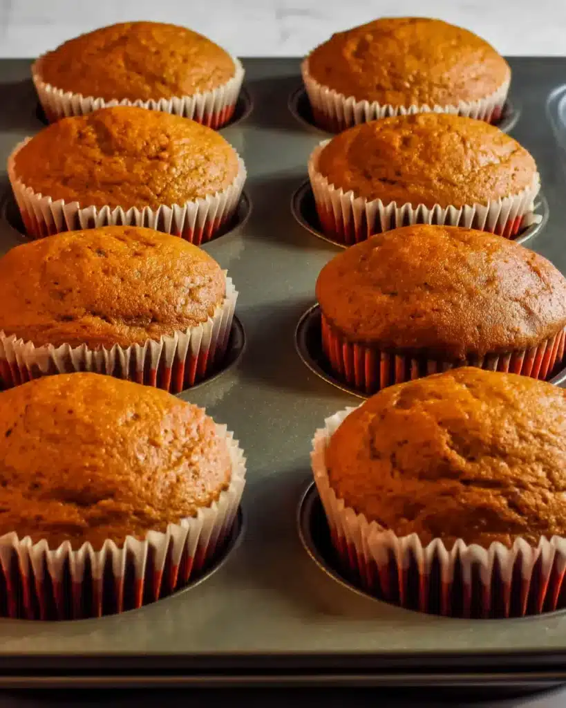 Freshly baked pumpkin cupcakes in orange and green liners cooling on a tray