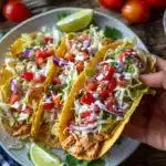 Hand holding a Slow Cooker Ranch Chicken Taco with fresh toppings and ranch drizzle