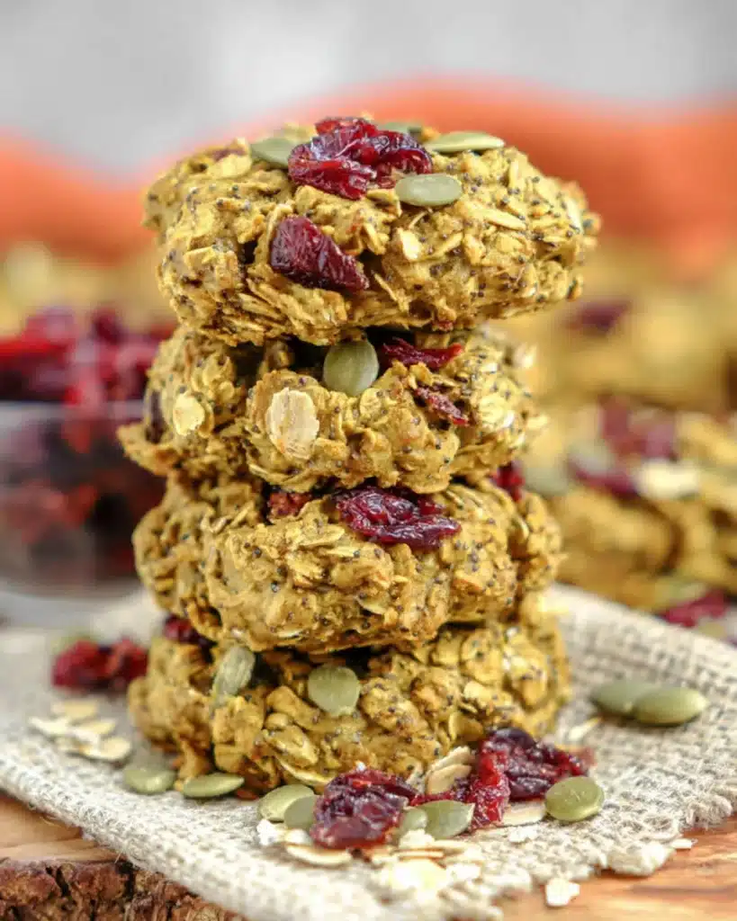 Stack of homemade pumpkin breakfast cookies with cranberries, oats, and seeds on a rustic surface.