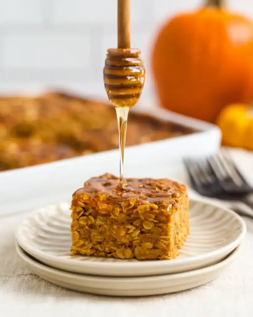 Honey being drizzled over a slice of pumpkin baked oatmeal on a white plate with fall background