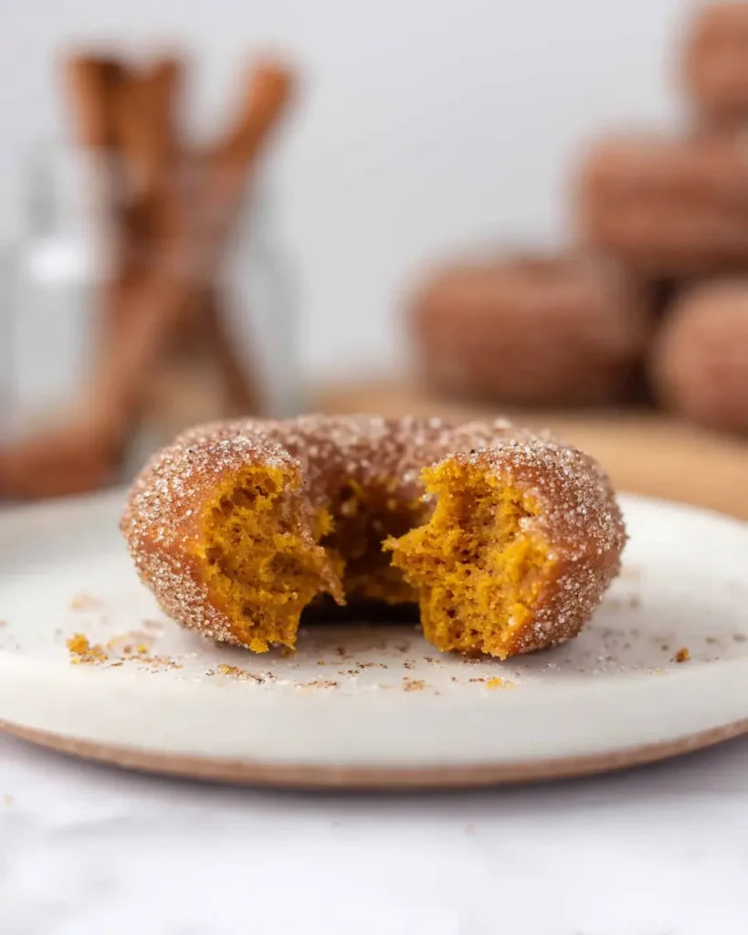 Broken cinnamon sugar pumpkin donut showing soft golden interior on white plate