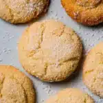 Soft keto cream cheese cookies with golden edges and powdered sweetener on a blue ceramic surface
