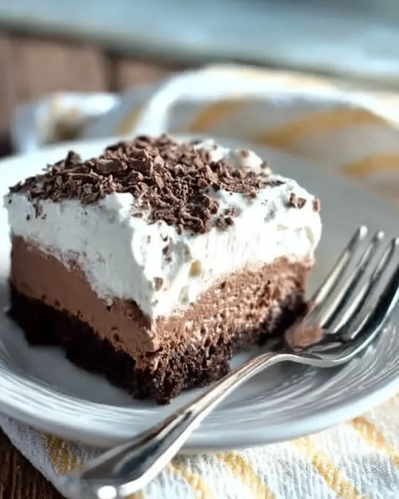 Close-up slice of French Silk Brownie with neat layers on white ceramic plate and striped cloth background.