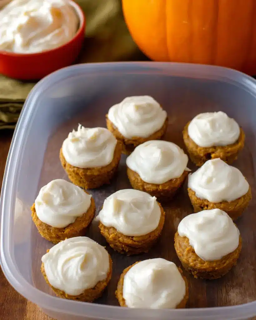 Plastic container filled with mini flourless pumpkin muffins topped with creamy frosting on rustic wood table
