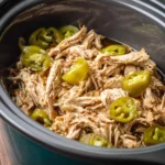 Slow cooker filled with shredded Mississippi chicken and whole banana peppers, juicy and tender.
