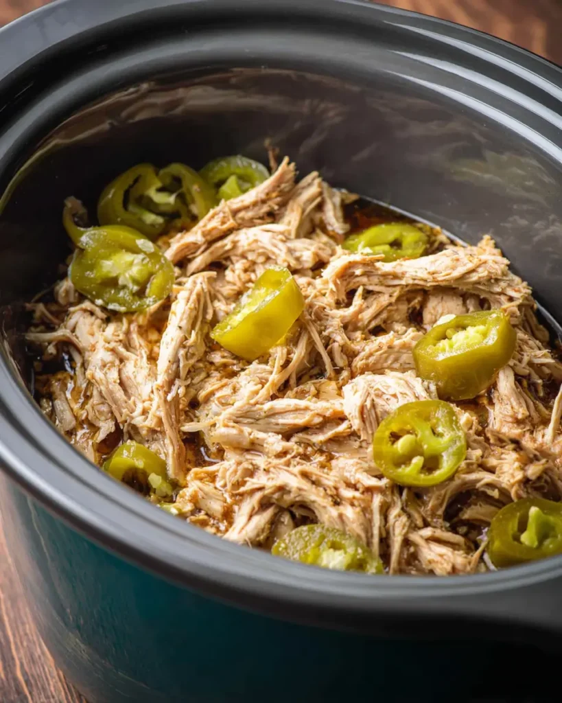 Slow cooker filled with shredded Mississippi chicken and whole banana peppers, juicy and tender.