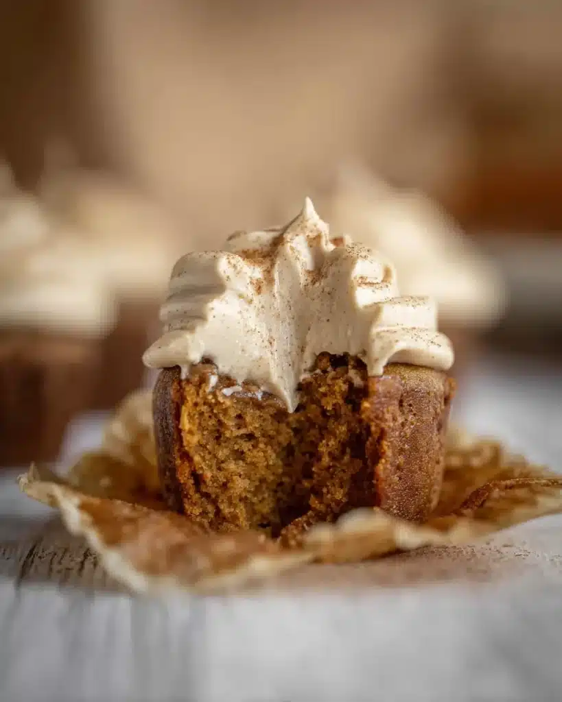 Close-up of a moist pumpkin cupcake with espresso frosting and cinnamon dusting, partially eaten.