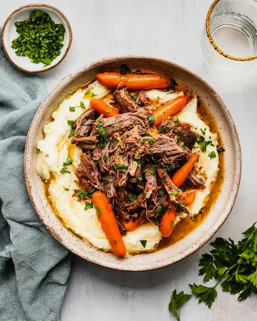 Overhead view of slow cooker garlic herb pot roast with carrots and gravy over mashed potatoes, garnished with fresh parsley