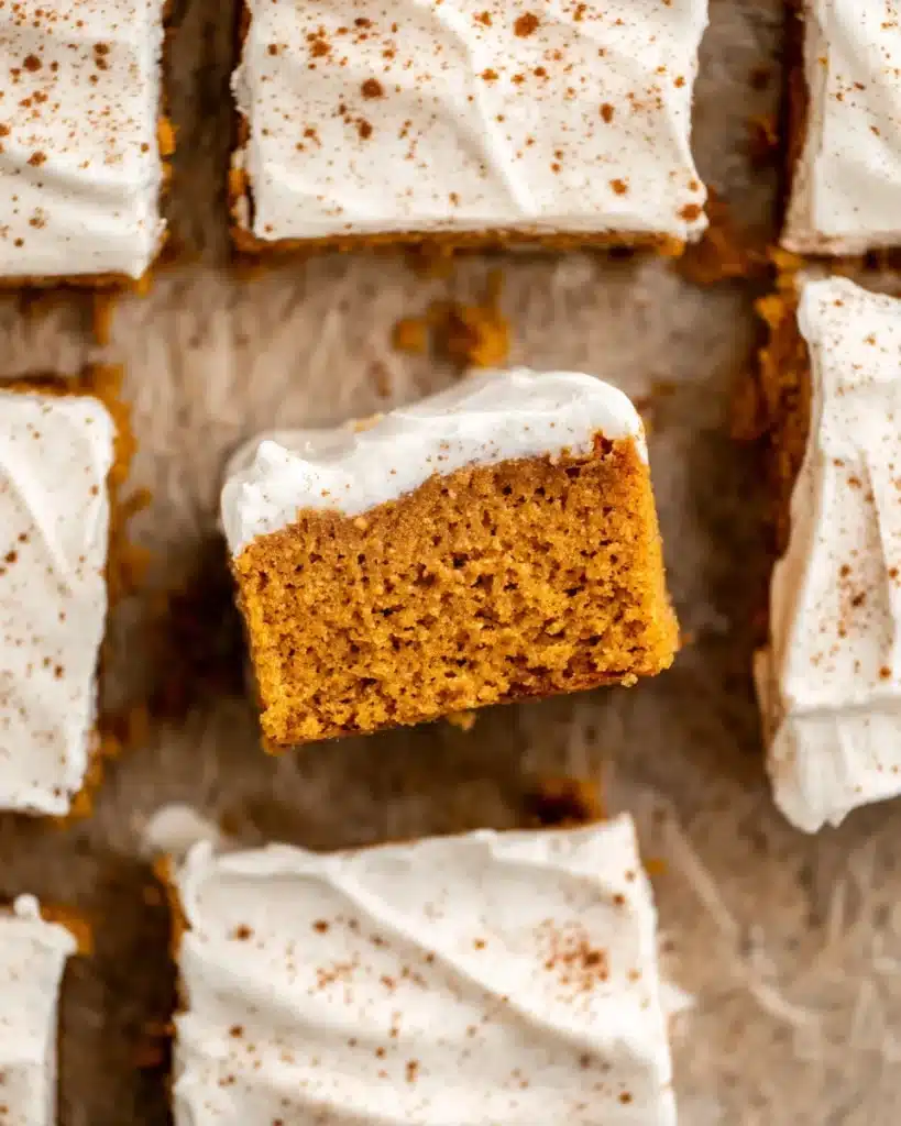 Top-down view of moist pumpkin bars with cream cheese frosting and cinnamon on parchment