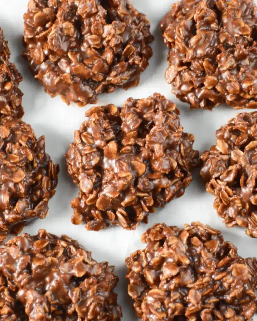 Close-up overhead shot of multiple gluten-free no bake cookies with chunky oat texture and glossy chocolate coating on a neutral background.