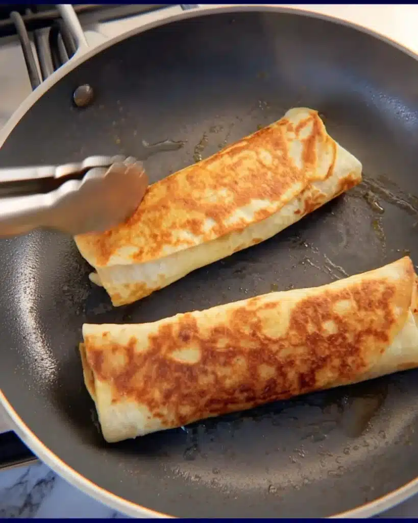 Flipping cheesy garlic chicken wrap in skillet until golden brown
