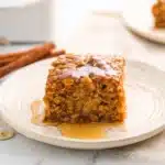 Slice of pumpkin baked oatmeal with syrup on a white plate, served on a cozy breakfast table